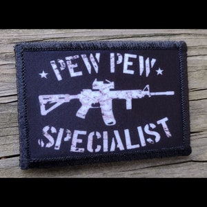 May include: Black and white embroidered patch with a white silhouette of a rifle and the text "*PEW PEW* SPECIALIST" on a black background.
