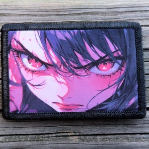 May include: A rectangular patch featuring a close-up anime-style illustration of a person's face. The eyes are bright pink, and the hair is dark purple. The patch has a black border.