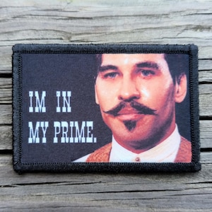 May include: Rectangular patch with a black border featuring a portrait of a man with a large mustache. The text "IM IN MY PRIME" is printed in white block letters on the left side of the patch.