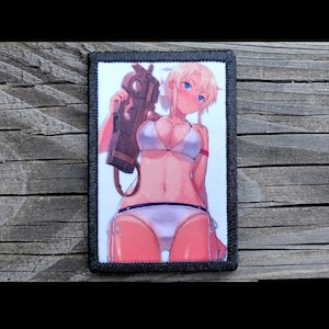 May include: Rectangular patch with a black border featuring an anime-style illustration of a woman in a white bikini holding a weapon. The woman has blonde hair and blue eyes. The background is white.