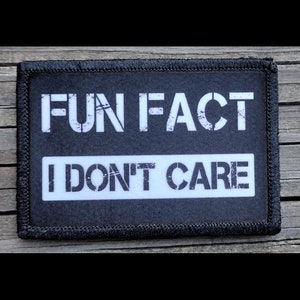 May include: Black rectangular patch with white text that reads "FUN FACT" above "I DON'T CARE". The patch has a black border and is likely made of fabric. The text is in a bold, stencil-style font.