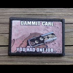 May include: A rectangular patch with the text "DAMMIT CARL YOU HAD ONE JOB..." above an image of a gun magazine with bullets. The patch has a black border and is set against a wood grain background.