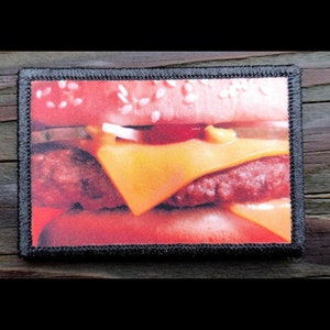 May include: Close-up of a cheeseburger with a sesame seed bun, a beef patty, melted cheese, and a red sauce.