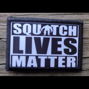 May include: Black and white embroidered patch with the text "SQUATCH LIVES MATTER" and a silhouette of a Bigfoot in the middle of the text.