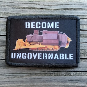 May include: A rectangular black patch with a stitched border featuring a yellow bulldozer illustration in the center. The text BECOME is printed in white above the bulldozer, and the text UNGOVERNABLE is printed in white below the bulldozer.