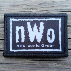 May include: A rectangular black patch with a white border. The patch features the text "nWo" in white, above the words "new world order" in white, all on a black background.
