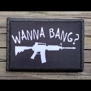 May include: Black and white patch with a white silhouette of a rifle and the text "WANNA BANG?" in white.