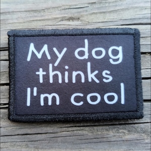 May include: A rectangular black patch with the text "My dog thinks I'm cool" in white. The patch has a black border and is set against a wooden background.
