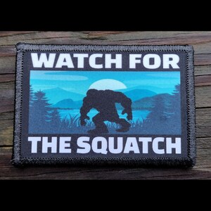 May include: A black and white patch with a blue and white background. The patch says "Watch for the Squatch" and features a silhouette of Bigfoot walking through a forest.