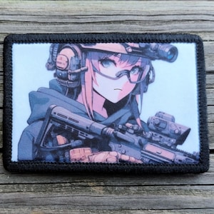 May include: A rectangular patch with a black border features an anime-style illustration of a person in tactical gear, holding a rifle. The character has pink and blue hair, wearing goggles and a headset. The background is light blue.