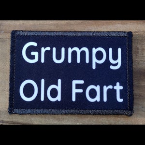 May include: A rectangular patch with the words "Grumpy Old Fart" in white block letters on a navy blue background. The patch has a black border with silver stitching.