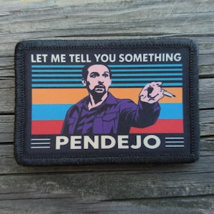 May include: A rectangular patch with a black border featuring a graphic of a person pointing a finger. The background has horizontal stripes in blue, orange, and red. The text reads LET ME TELL YOU SOMETHING at the top and PENDEJO at the bottom.