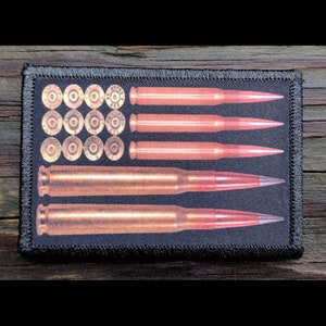 May include: A rectangular black patch with a design resembling the American flag, featuring bullet casings and bullets. The top section has bullet casings, and the stripes are represented by bullets with red tips.