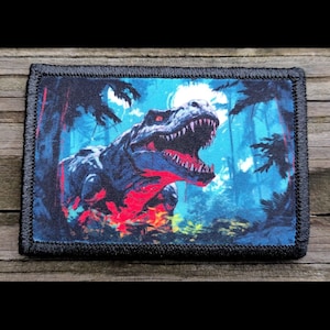 May include: A black and blue embroidered patch featuring a roaring Tyrannosaurus Rex dinosaur in a jungle setting.