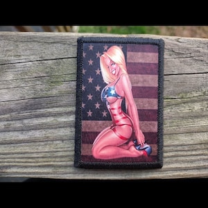 May include: A rectangular patch featuring a cartoon illustration of a woman in a patriotic outfit, set against a backdrop of the American flag. The woman is blonde, wearing a star-spangled bikini and red garter straps. The patch has a black border.