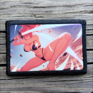 May include: A rectangular patch with a black border features a vibrant illustration of a female anime character wielding a sword. The character is depicted in a dynamic pose with a background of light and shadow.
