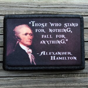 May include: A rectangular patch with a portrait of Alexander Hamilton and the quote "Those Who Stand For Nothing, Fall For Anything." The patch has a black border and is set against a dark background.