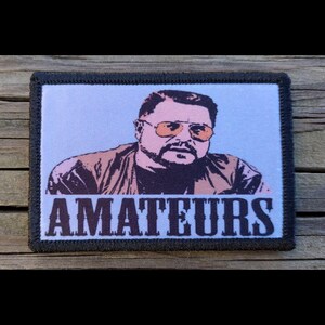 May include: Rectangular patch with a portrait of a man wearing sunglasses, with the word "AMATEURS" in white block letters. The patch has a black border and a light blue background.
