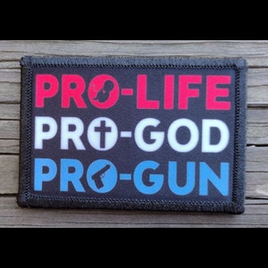 May include: A rectangular patch with the words "PRO-LIFE", "PRO-GOD", and "PRO-GUN" in red, white, and blue. The patch features a black background and a black stitched border. The words are in a bold, sans-serif font.