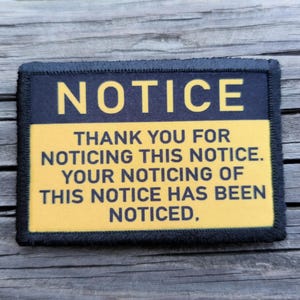 May include: A rectangular patch with the word "NOTICE" in large yellow letters on a black background. Below, yellow text reads: "THANK YOU FOR NOTICING THIS NOTICE. YOUR NOTICING OF THIS NOTICE HAS BEEN NOTICED."