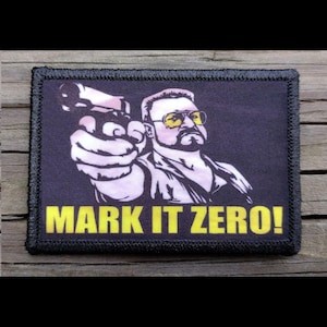 May include: A rectangular patch with a black border and a black background. The patch features a white and black illustration of a man with yellow-tinted glasses pointing a gun. The text "MARK IT ZERO!" is in yellow.