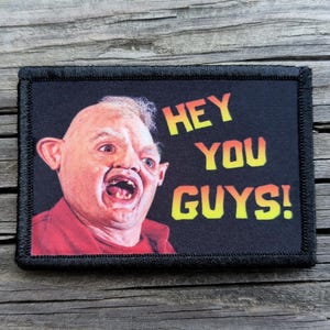 May include: A rectangular patch featuring a character's face with an open mouth and the text "HEY YOU GUYS!" in yellow and orange. The character is wearing a red shirt. The patch has a black border.