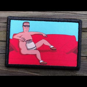 May include: A rectangular patch featuring a cartoon image of a man sitting on a red couch. The man is wearing glasses and holding a jar. The background is light blue, and the patch has a black border.