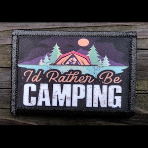 May include: A rectangular patch with a black border and the text "I'd Rather Be CAMPING". The patch features a camping scene with a tent, trees, a lake, and a sunset. The background is dark with a purple and blue sky.
