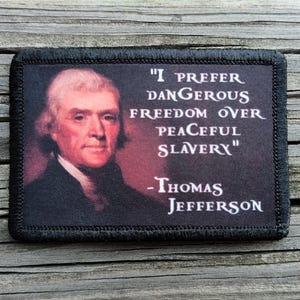 May include: A rectangular patch with a portrait of Thomas Jefferson and the quote "I prefer dangerous freedom over peaceful slavery." The patch has a black border and is set against a wood grain background.
