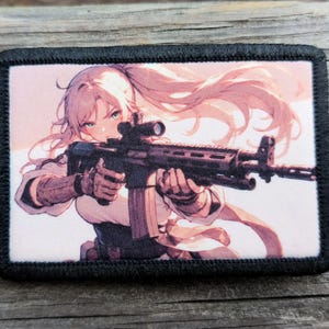 May include: Rectangular patch with a black border featuring an anime-style illustration of a person holding a rifle. The person has long, flowing pink hair and is wearing a white and brown outfit. The rifle has a scope.