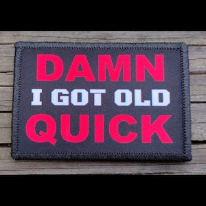 May include: A rectangular black patch with the words "DAMN I GOT OLD QUICK" in red and white lettering. The patch has a black border with stitched edges. The text is centered on the patch.
