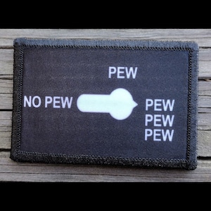 May include: Black rectangular patch with white text and a toggle graphic. The text reads "NO PEW" on the left, "PEW" above the toggle, and "PEW PEW PEW" on the right. The patch has a black stitched border.