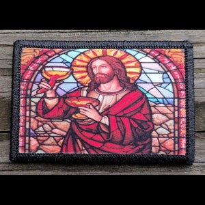 May include: A stained glass window image of Jesus holding a chalice. The image is framed in black fabric with a stitched border.