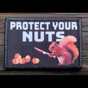 May include: A rectangular patch with the text "PROTECT YOUR NUTS" in white letters on a black background. A cartoon squirrel holding a bloody knife is on the right. Acorns are at the bottom left. The patch has a black border.