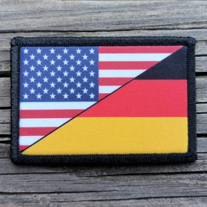 May include: Rectangular patch featuring a split design of the American and German flags. The American side displays the stars and stripes, while the German side shows the black, red, and gold colors. The patch has a black border.