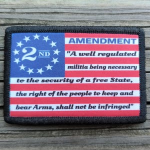 May include: A rectangular patch featuring a stylized American flag design. The upper left corner has a blue field with white stars and the number "2ND". Red and white stripes make up the rest of the flag, with text that reads "AMENDMENT" and the Second Amendment.