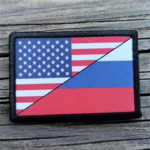 May include: Rectangular patch featuring a split design. The left side displays the American flag with stars and stripes, while the right side shows the Russian flag's colors. The patch is bordered with black stitching.