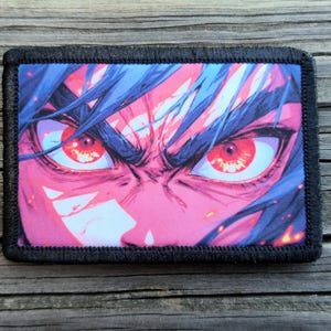 May include: A rectangular patch featuring an anime-style illustration of a character's face. The character has intense red eyes, blue hair, and a pink complexion. The patch is bordered with black stitching, suitable for sewing or attaching to fabric.