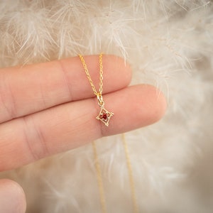 Könnte beinhalten: Eine goldene Kettenkette mit einem kleinen, roten Edelstein-Anhänger in Form eines Diamanten.