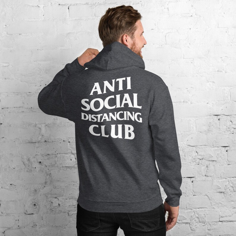 Peut inclure: Un sweat &agrave; capuche gris fonc&eacute; avec l'inscription blanche "ANTI SOCIAL DISTANCING CLUB" au dos. Le sweat &agrave; capuche a une capuche et des manches longues. La personne sur l'image porte le sweat &agrave; capuche.