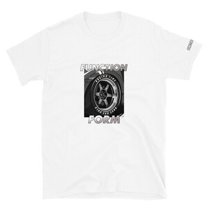 May include: White t-shirt featuring a graphic of a car wheel with the words "FUNCTION" and "FORM" in a bold font. The wheel graphic is in grayscale, with the word "RACING TIRE" visible on the tire. The word "FUNCTION" is also printed on the sleeve.
