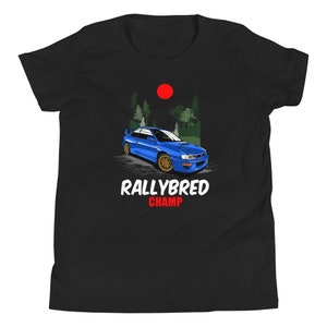 May include: Black t-shirt with a blue rally car graphic, gold wheels, and a forest and red sun backdrop. The text "RALLYBRED CHAMP" is displayed in white and red.