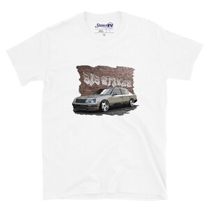 Könnte beinhalten: Weißes T-Shirt mit einem Aufdruck eines silbernen Autos mit dem Text "Old Stance" vor einem Hintergrund aus Ziegeln.