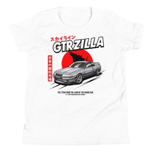 May include: White t-shirt with a silver car graphic, the text "GTRZILLA", and a red sun design. Japanese text and the phrase "THE TITAN FROM THE LAND OF THE RISING SUN" are also present on the shirt.