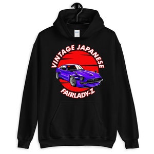 May include: Black hooded sweatshirt with a graphic of a purple vintage Fairlady-Z car set against a red sun. The text "VINTAGE JAPANESE FAIRLADY-Z" is printed in white. The sweatshirt has a front pocket and a drawstring hood. The design is reminiscent of Japanese car culture.