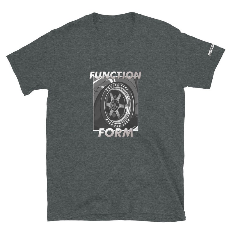 Op de afbeelding: Donkergrijs t-shirt met een afbeelding van een autowiel en de woorden "FUNCTION" en "FORM" in een rechthoekige lijst. De wielafbeelding is in grijstinten en wit, met de woorden "RACING TIRE" en andere tekst zichtbaar.