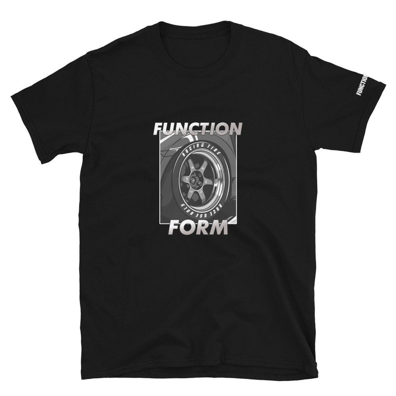 Op de afbeelding: Zwart T-shirt met korte mouwen met een afbeelding van een autowiel en de woorden "FUNCTION" en "FORM" in een zilverkleurig, omlijnd lettertype. De woorden "RACING TIRE" zijn ook zichtbaar. Het woord "FUNCTION" staat op de mouw.