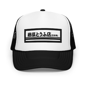 May include: Black and white trucker hat with a rectangular graphic on the front. The graphic features Japanese text in black within a white rectangle, outlined in black. The hat has a white front panel and a black mesh back.