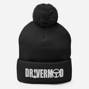 May include: Black beanie with a large, fluffy pom-pom on top. The front of the hat features the white text "DRIVERMOD" with a steering wheel graphic. A warm and stylish winter accessory.