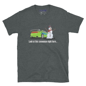 May include: A dark heather grey t-shirt with a green and blue car and a snowman with a red scarf and black top hat. The text "Look at this snowman right here..." is printed below the image.